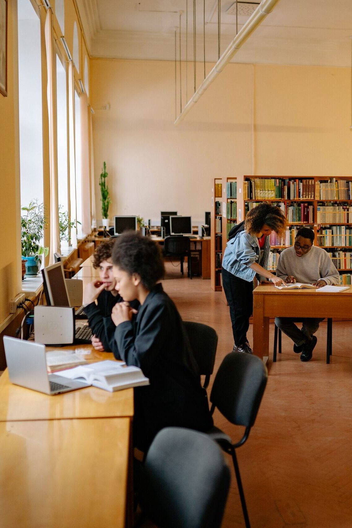 Students studying and collaborating in a university library setting with bookshelves and desks.